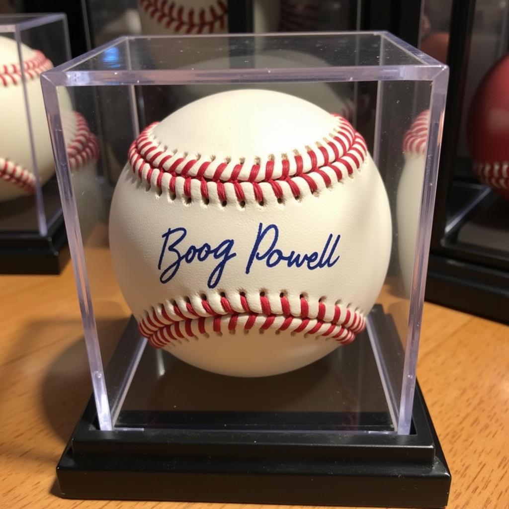 A Boog Powell signed baseball displayed in a clear, UV-protected acrylic case.  The case is positioned on a shelf alongside other baseball memorabilia, showcasing the baseball as part of a carefully curated collection.